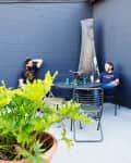 Two men sitting at a round metal table in a patio with a potted plant and dark blue walls.