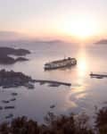 Ferry sailing at sunset near a coastal town with islands in the background.