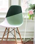Two modern chairs with wooden legs by a window, one with a green and white design, next to a small round table and a plant.