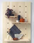 Wooden pegboard with shelves holding a plant, black and white cloth, glass bottle, and ceramic fish dish.