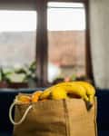 Jute bag filled with bananas and oranges on a table near a window with potted plants.