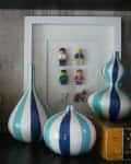 Striped blue and white vases in front of framed LEGO minifigures on a wooden shelf.