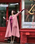 Woman in pink coat and hat joyfully posing outside Lutzi's Butcher Shop with vintage signage.