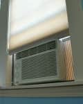 Window air conditioner installed between two windows with beige blinds.