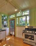 Bright kitchen with green-framed windows, stainless steel sink, and gas stove, overlooking a lush garden.