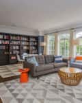 Spacious living room with gray sectional sofa, bookshelves, large windows, and geometric rug.