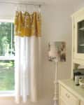 Yellow floral curtains and a decorative lamp beside a cream cabinet in a bright room with a window view of greenery.