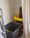 Vacuum cleaner and storage bin in a small closet with curtain.