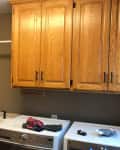 Laundry room with wooden cabinets, sink, and washer-dryer set, clothes on top.