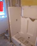 Bathroom under renovation with exposed wall studs, old bathtub, and debris on the floor.