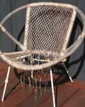 Worn wicker chair with frayed seat and backrest on a wooden deck.