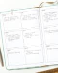 Open planner with monthly sections, pen, paper clips, and ruler on a white surface.