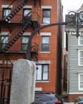 Narrow gray house between two red brick buildings, viewed through an ornate iron archway.