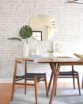 Dining area with wooden table and chair, round mirror, and decorative plants on a textured wall.