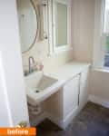 Small bathroom with a white sink, round mirror, and cabinet under a window.