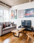 Modern living room with gray sofa, colorful pillows, wooden coffee table, TV, and abstract wall art.
