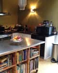 Kitchen with stainless steel island, fruit bowl, open shelving with books, and appliances on black countertops.