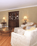 Living room with white sofas, glass coffee table, wooden cabinet, and two table lamps on side tables.