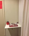 Small corner desk with a red pen holder, laptop with stickers, and white curtain backdrop.