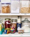 Organized pantry shelves with labeled jars of oats, pasta, polenta, spices, and baking ingredients.
