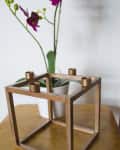 Bronze cube candle holder on wooden table with purple orchid in white pot.