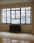 Empty room with large grid windows, beige walls, and a dark radiator under the window.