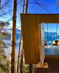 Treehouse with open door, revealing a cozy interior with chairs and a table, overlooking a scenic mountain view.