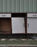 Worn wooden sideboard with peeling white paint and open doors, set against a corrugated metal wall.
