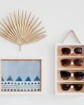 Gold palm leaf decor, framed blue geometric art, and sunglasses display on a white wall.