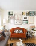 Living room with orange sofa, gallery wall of framed art, gray couch, globe on side table, and bar cart with bottles.