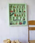 Green wall-mounted alphabet shelf with small toys, next to a wooden chair and a bucket of stuffed animals.