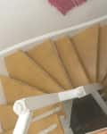 Top view of narrow, curved wooden staircase with white railing and beige steps.