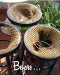 Three black bar stools with damaged woven seats next to a green fern plant.
