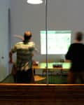 Two people playing a video game projected on a wall in a room with a table and chairs.