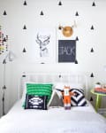 Kids' bedroom with triangle wall pattern, white bed, colorful pillows, fox plush toy, and green side table with books.