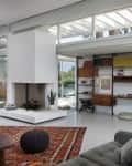 Modern living room with a white fireplace, gray sofa, patterned rug, and wall shelves displaying books and decor.