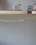 Wooden shelf with jars and a basket, above a string of colorful triangular bunting.