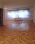 Empty room with parquet flooring, white walls, and large windows.