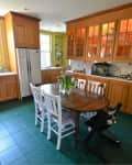 Kitchen with wooden cabinets, green tile floor, round table, and white chairs.