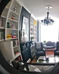 Modern living room with curved bookshelves, black chandelier, and armchairs reflected in a circular mirror.
