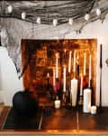 Fireplace with lit candles, black pumpkin, birdcage on stand, and skull garland draped with black netting.