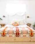 Bedroom with a colorful geometric blanket, plants, wooden side tables, and wall art.