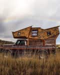 Vintage truck with a wooden camper in a grassy field under a rainbow.