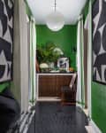Hallway with green walls, black and white art, dark tiled floor, wooden cabinet, and plants.