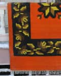Orange and black woven rug with yellow floral pattern draped over a snowy porch railing.