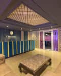Lobby with blue and yellow reception desk, patterned walls, beige sofas, and a glass door with pink accents.