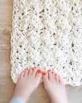 Feet with red toenails on a chunky knit white rug on wooden floor.