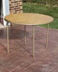 Round folding table with metal legs on a brick patio near a brick wall and grassy yard.