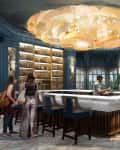 Elegant bar with a large chandelier, blue walls, and patrons seated around a white marble counter.