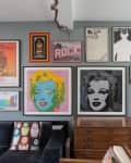 Gallery wall with colorful pop art, including Marilyn Monroe prints, above a dark sofa and wooden cabinet.